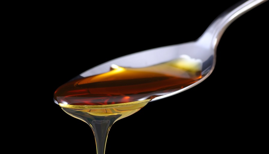 Syrup dripping off a spoon on black background